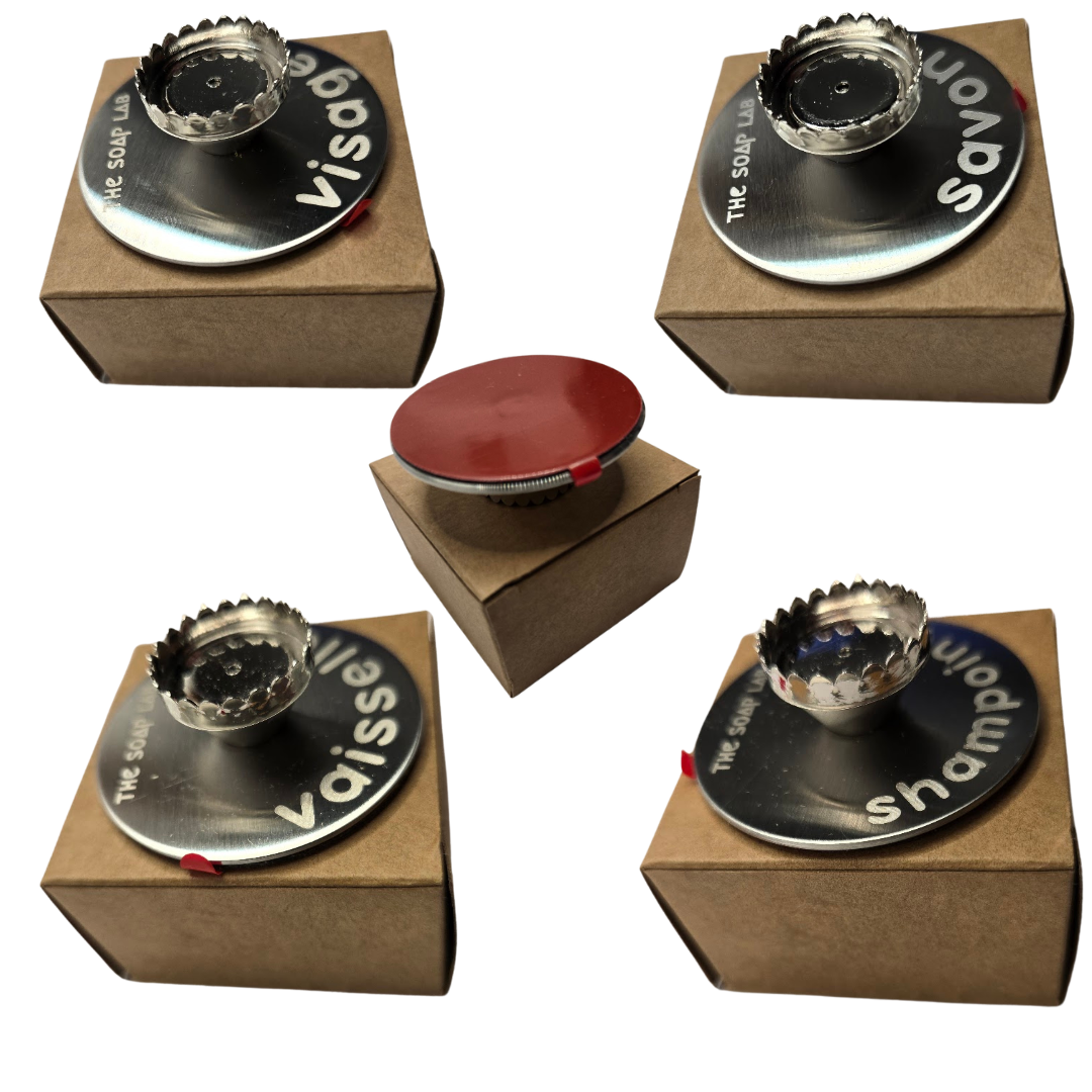 porte savon mural aimanté, 4 versions avec identification gravée sur le porte savon : Savon / Vaisselle / Shampoing / Visage. Positionnés sur leurs boîtes en carton et vus de 3/4 haut. 